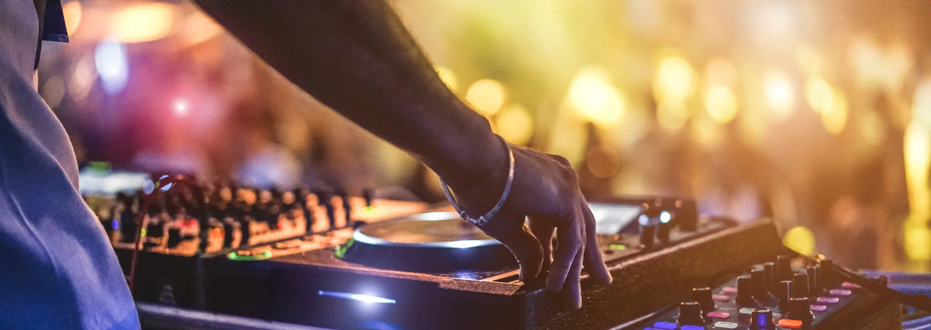 Ein DJ bei der Arbeit und im Hintergrund tanzende Menschen und bunte Lichter