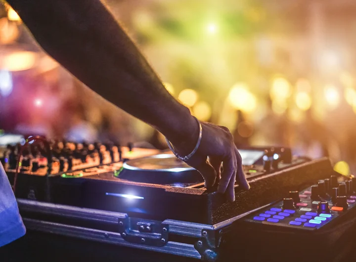 Ein DJ bei der Arbeit und im Hintergrund tanzende Menschen und bunte Lichter