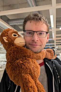 Profilfoto von Sergej, Mann posiert lächelnd mit einem Plüschtier um dem Hals