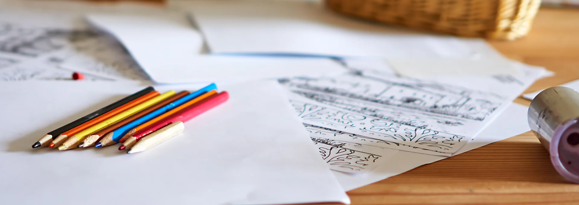 Colobell Person sitzt am Tisch und malt, auf dem Tisch liegen Stifte und Papier