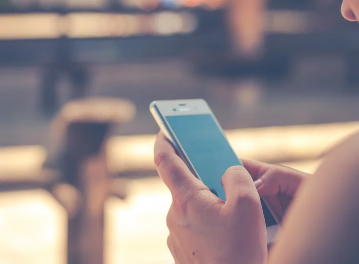 Bild zeigt ein Smartphone in der Hand einer Frau, der Hintergrund ist unscharf