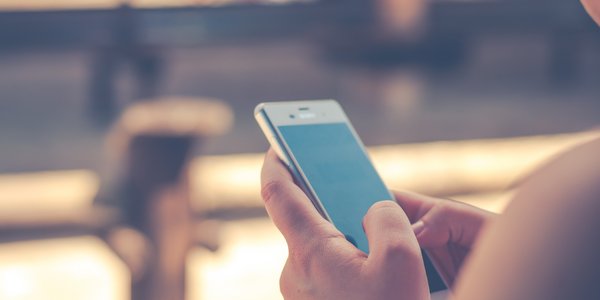 Bild zeigt ein Smartphone in der Hand einer Frau, der Hintergrund ist unscharf