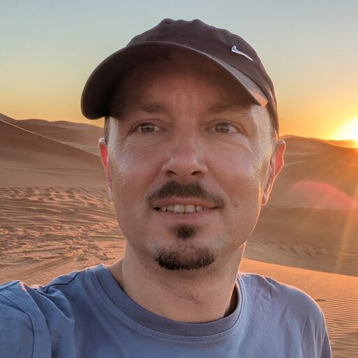 Profilfoto von Robert, Mann mit Bart und Käppi bei Sonnenuntergang und lächelt in die Kamera