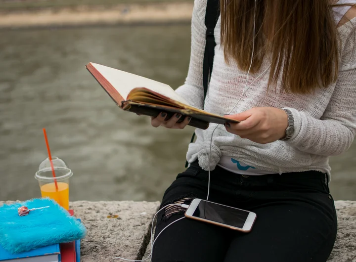 Eine junge Frau sitzt am Wasser mit einem Buch in der Hand