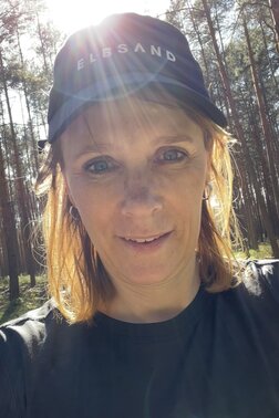 Profilfoto von Patricia, Frau mit Käppi schaut freundlich in die Kamera, Hintergrund zeigt Bäume
