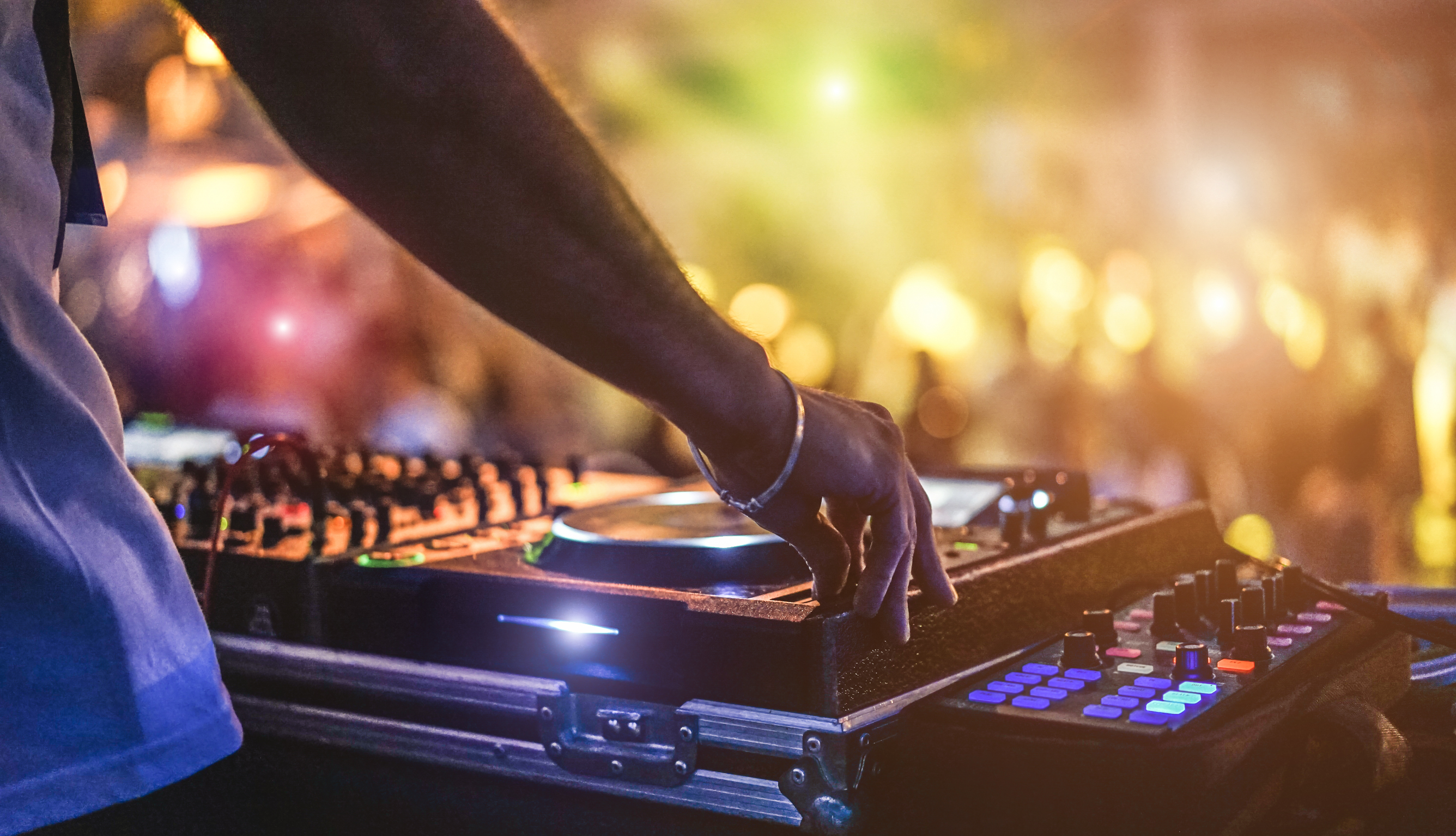 Ein DJ bei der Arbeit und im Hintergrund tanzende Menschen und bunte Lichter